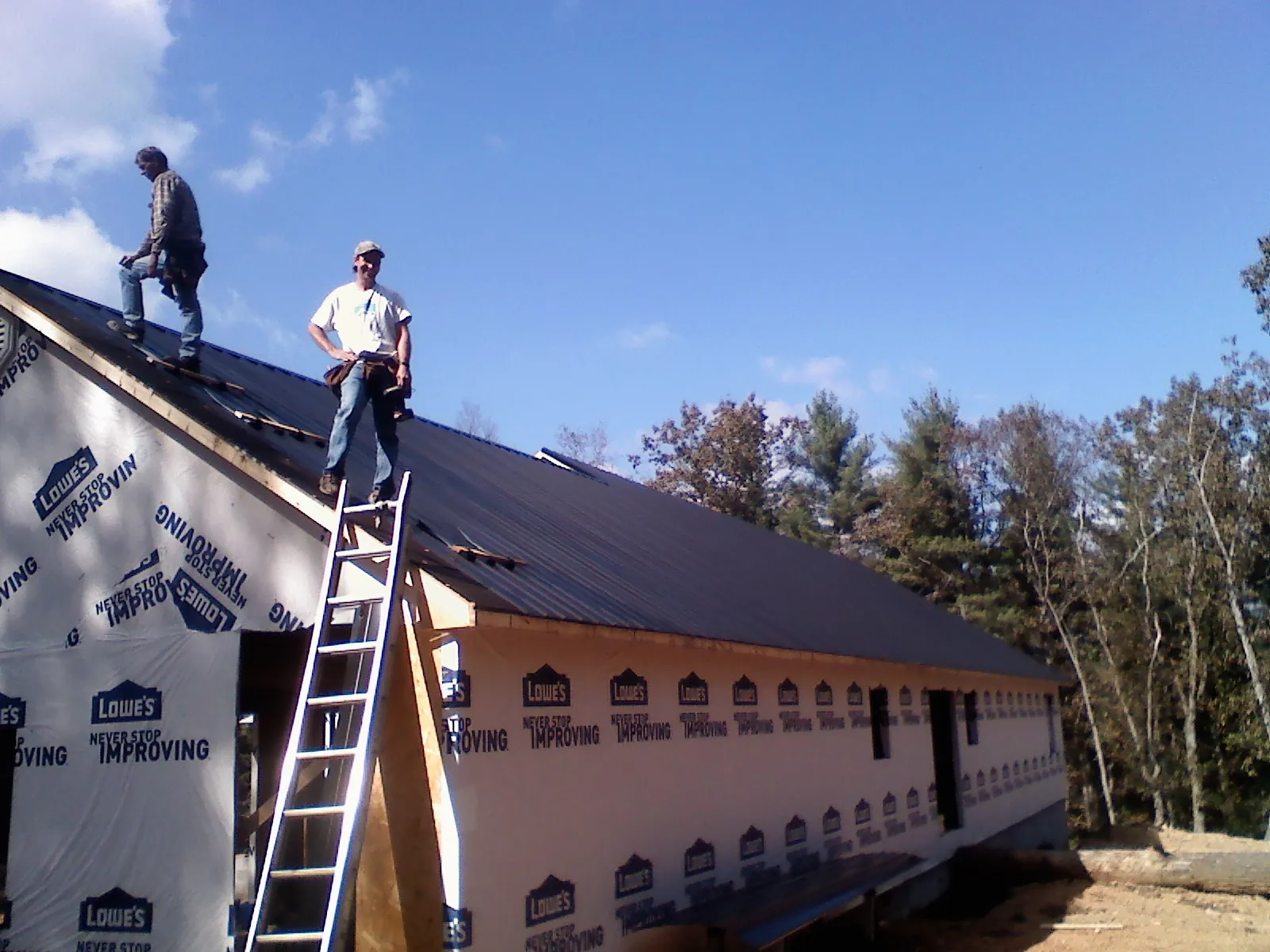 Two roofers standing on a long dark metal roof over a wrapped building in Quantico